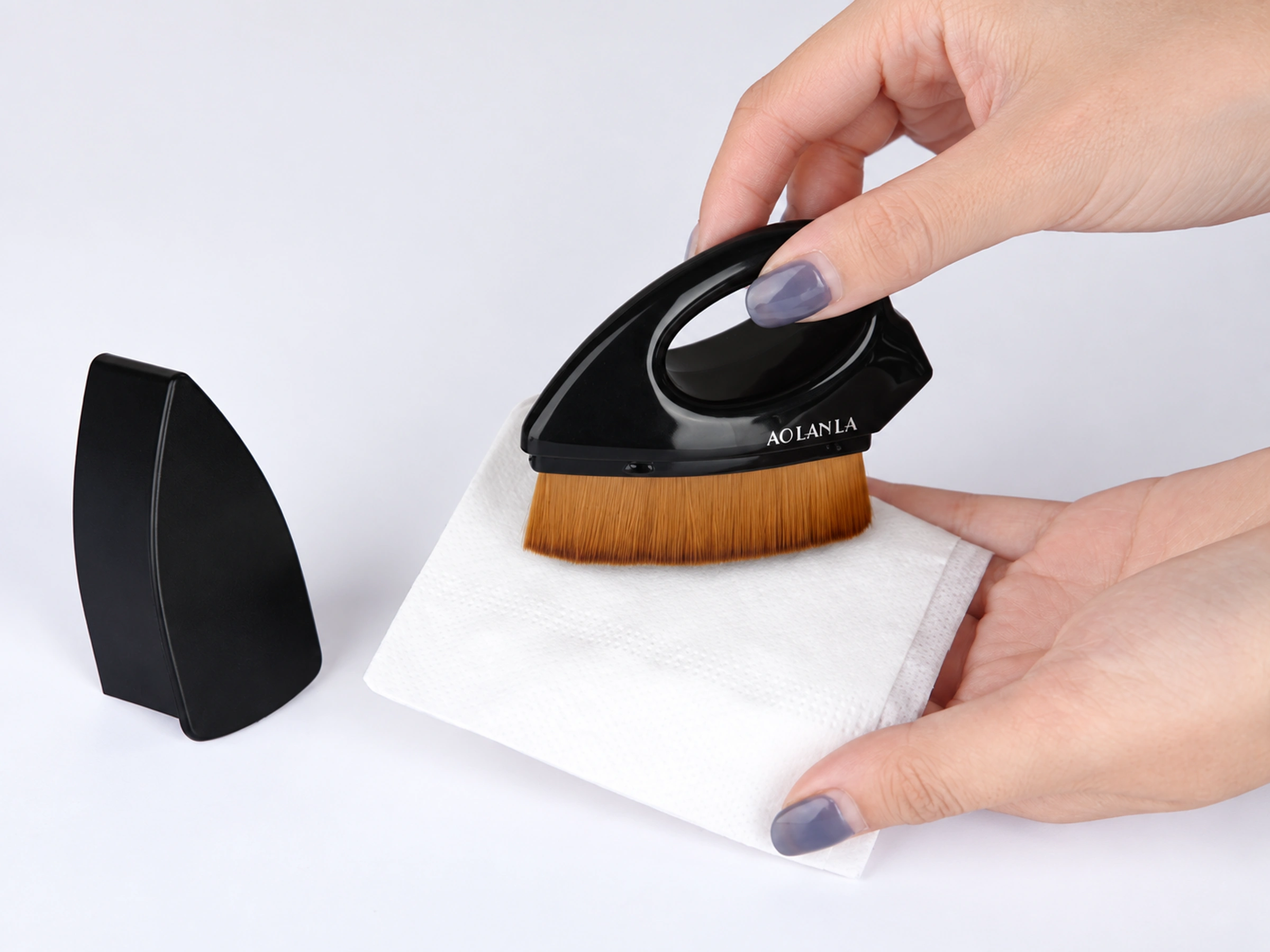 Original care demonstration with two hands wiping the brush face on a white absorbent sheet, with the separate holder beside it