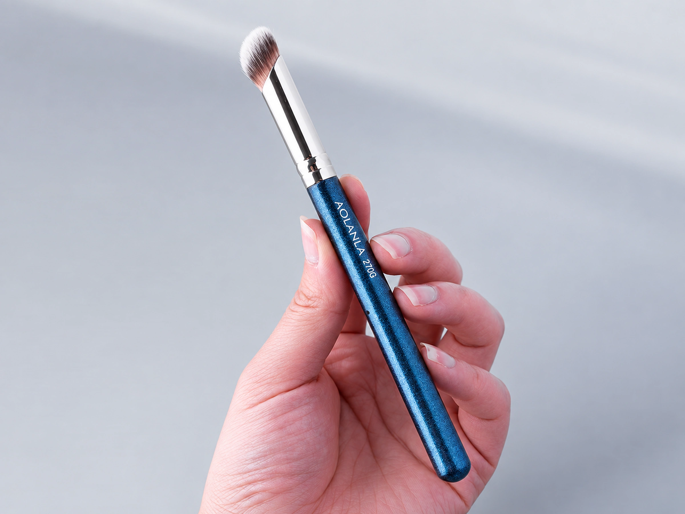 Original 270G angled concealer brush held in a hand, silver copper ferrule and blue grip