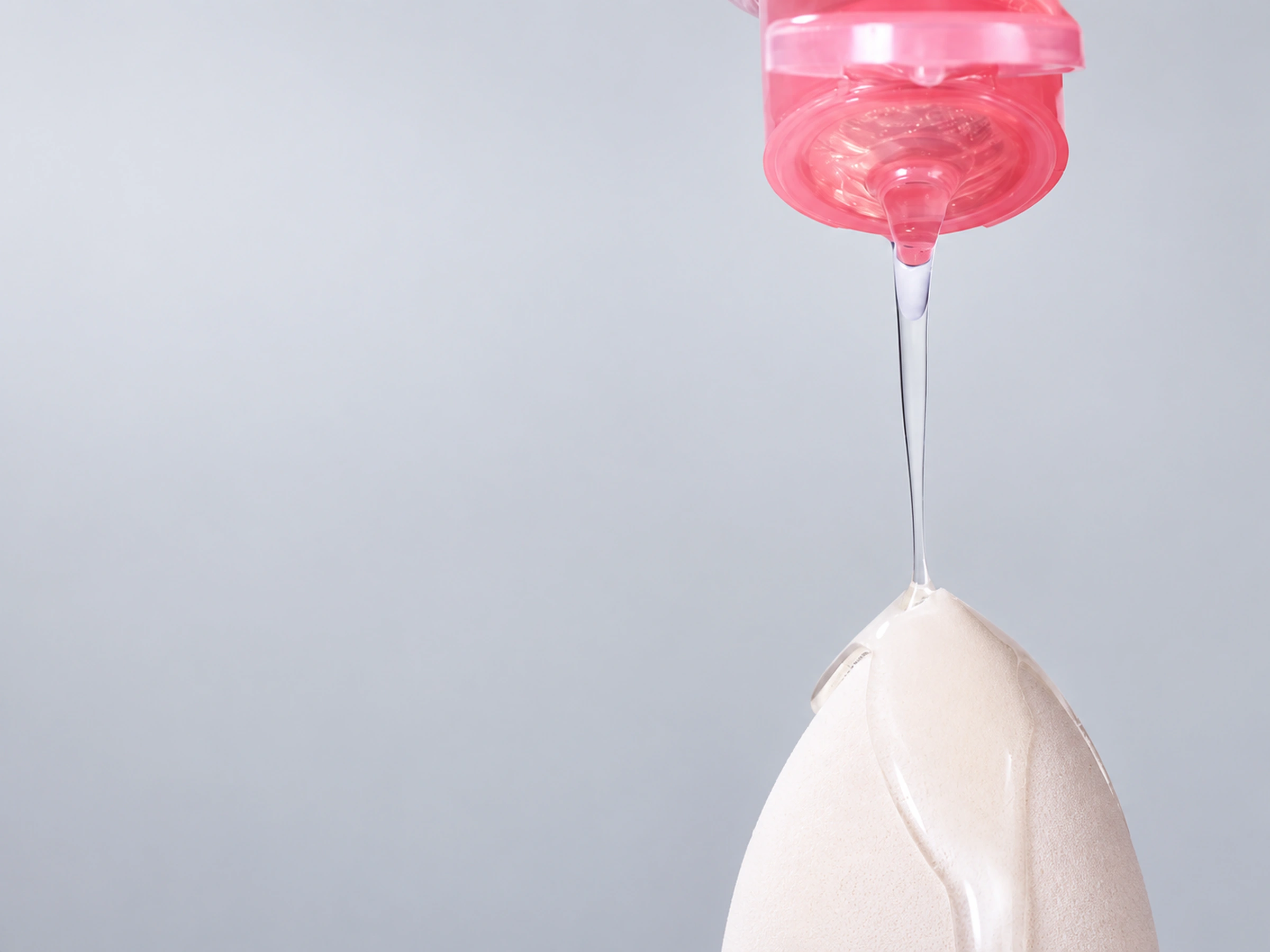 Clear cleanser flowing from the actual pink bottle onto a makeup sponge