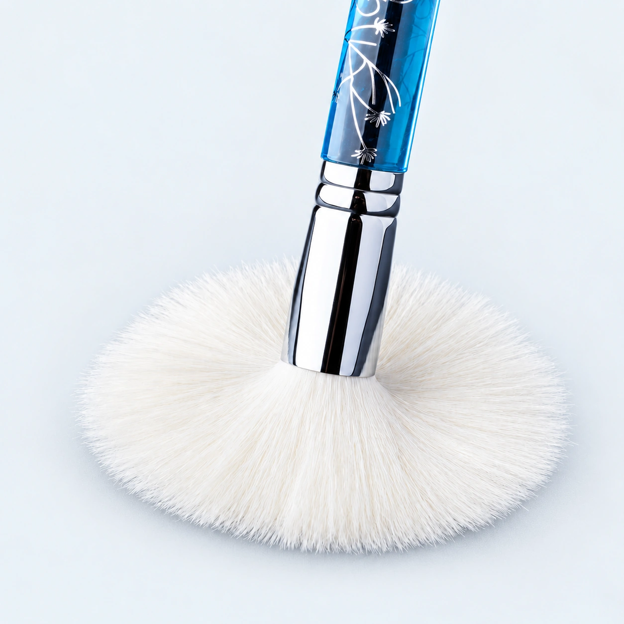 Fine ivory goat-hair powder brush flexing naturally, with a polished silver ferrule and patterned ice-blue handle