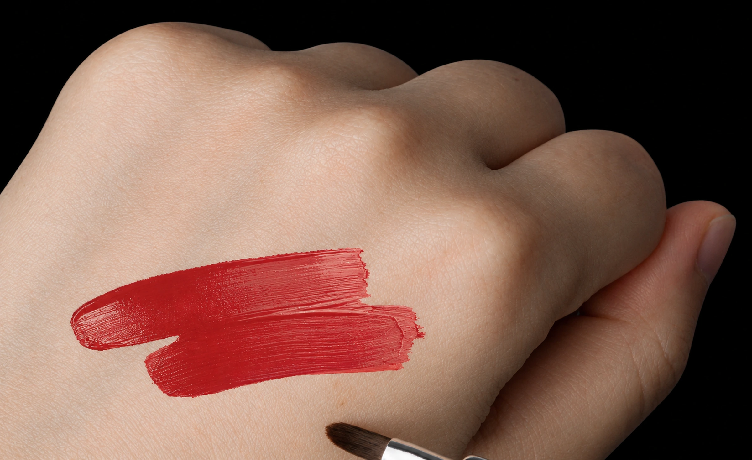 Actual red cream-colour strokes on the back of a hand beside the rounded dark lip-brush tip