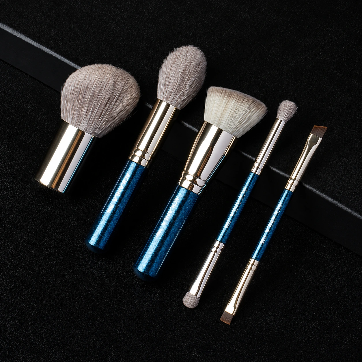 Five blue and silver travel brushes arranged diagonally on black fabric
