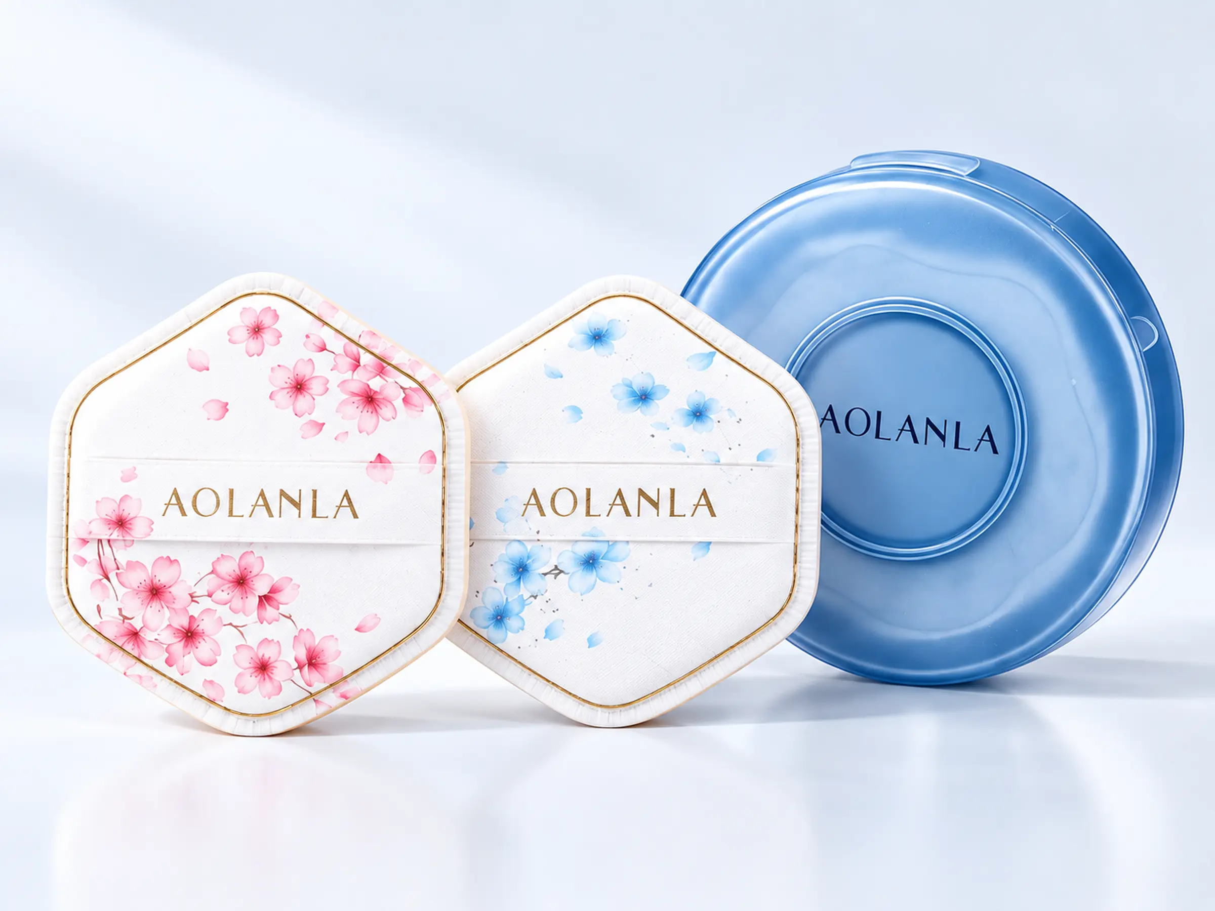 Pink and blue Sakura dual-use makeup puffs beside their round translucent blue storage case